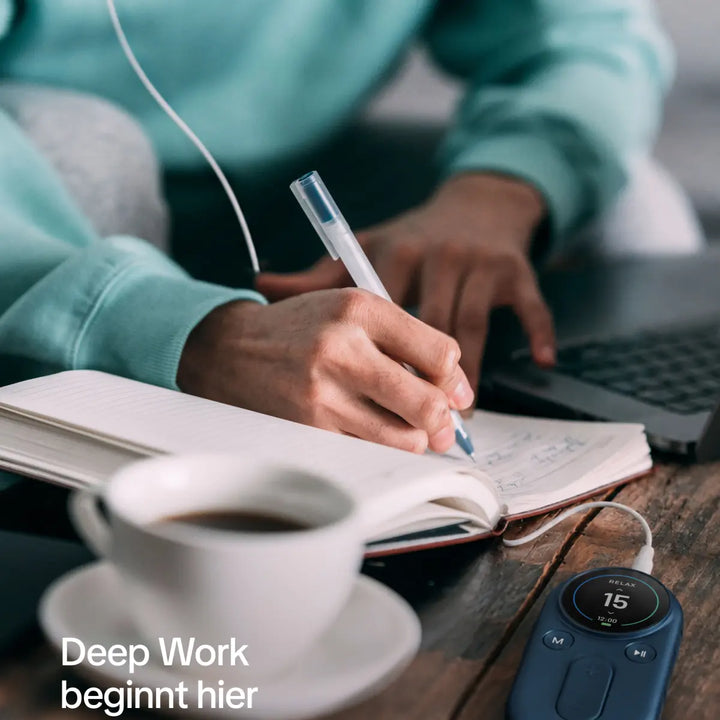 Person writing notes beside a laptop, coffee cup, and focus timer.