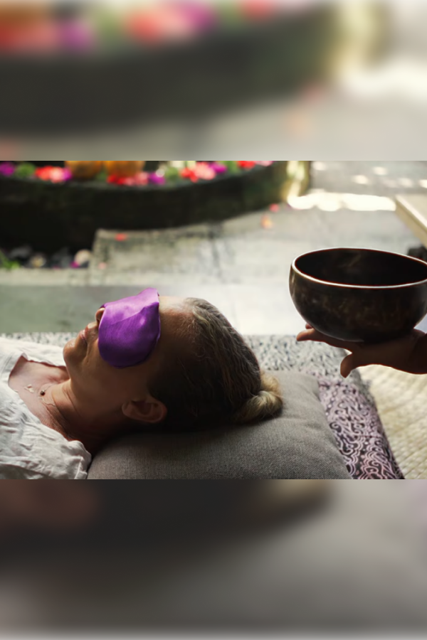 Woman with an eye mask receiving a sound bath with a singing bowl, in a peaceful wellness setting